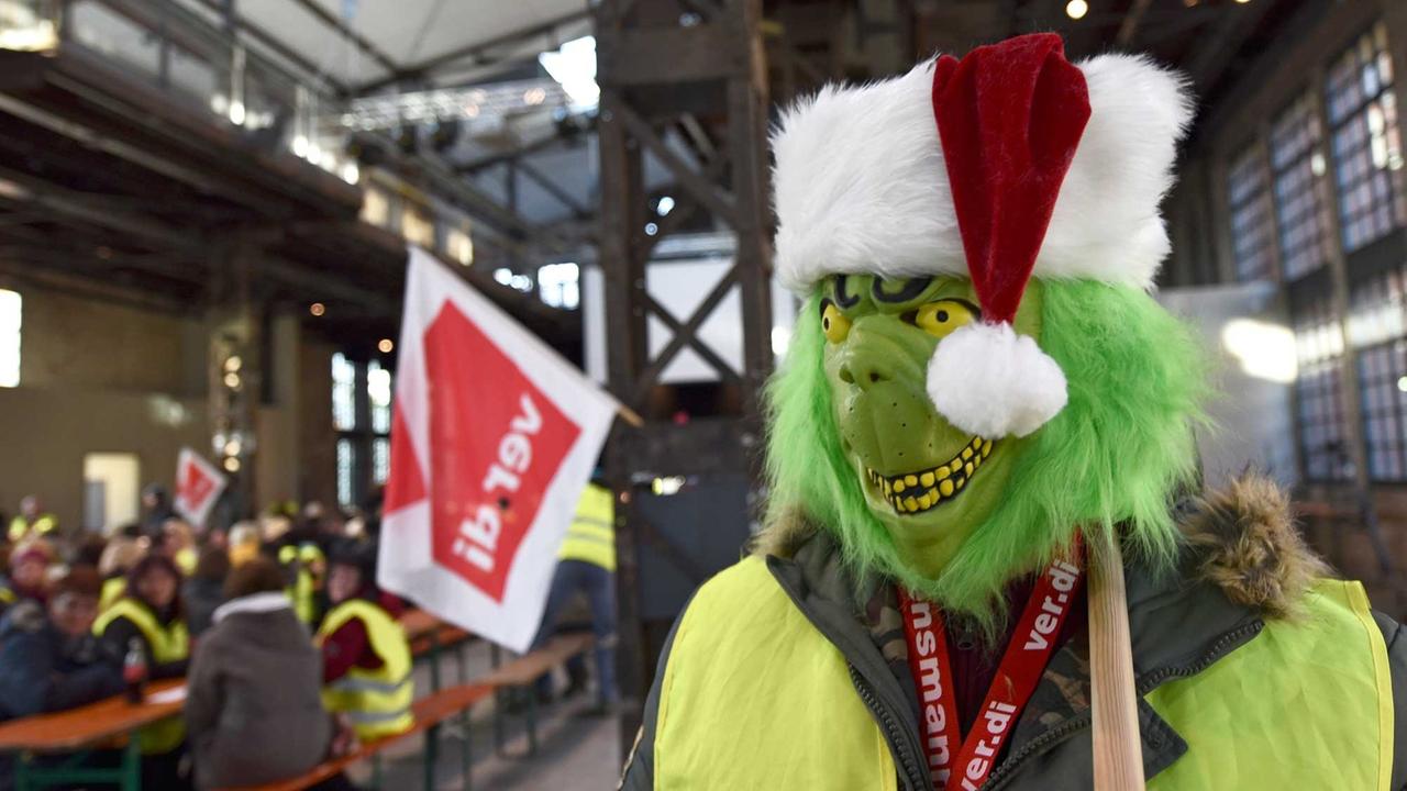 Verkleidet mit einer Grinch-Maske geht am 15.12.2014 ein Mann auf der Streikversammlung von Amazon-Mitarbeitern in Bad Hersfeld (Hessen) durch das Streiklokal. Verkleidet mit einer Grinch-Maske geht am 15.12.2014 ein Mann auf der Streikversammlung von Amazon-Mitarbeitern in Bad Hersfeld (Hessen) durch das Streiklokal.