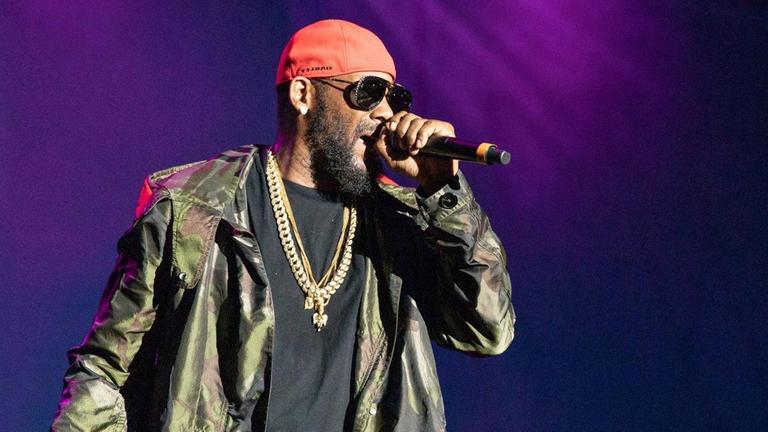 R. Kelly rappt in ein Mikrofon, in seiner Hand trägt er ein Whiskeyglas und Zigarre. R. Kelly rappt in ein Mikrofon, in seiner Hand trägt er ein Whiskeyglas und Zigarre.