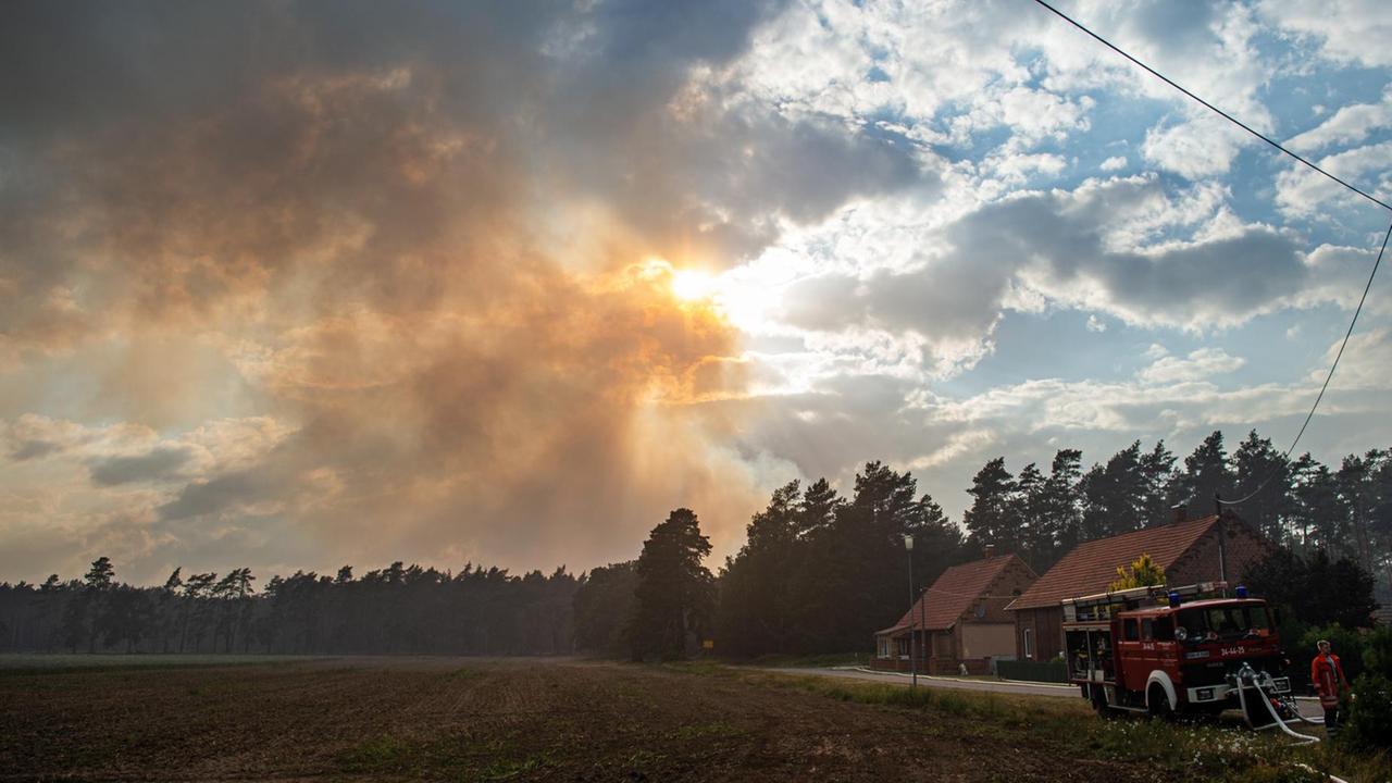 In Mecklenburg-Vorpommern, Hohen Woos, schützen Feuerwehrleute Häuser, deren Bewohner das Gebiet verlassen mussten, während Rauch in den Abendhimmel steigt In Mecklenburg-Vorpommern, Hohen Woos, schützen Feuerwehrleute Häuser, deren Bewohner das Gebiet verlassen mussten, während Rauch in den Abendhimmel steigt