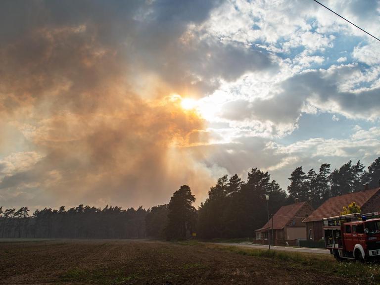 In Mecklenburg-Vorpommern, Hohen Woos, schützen Feuerwehrleute Häuser, deren Bewohner das Gebiet verlassen mussten, während Rauch in den Abendhimmel steigt