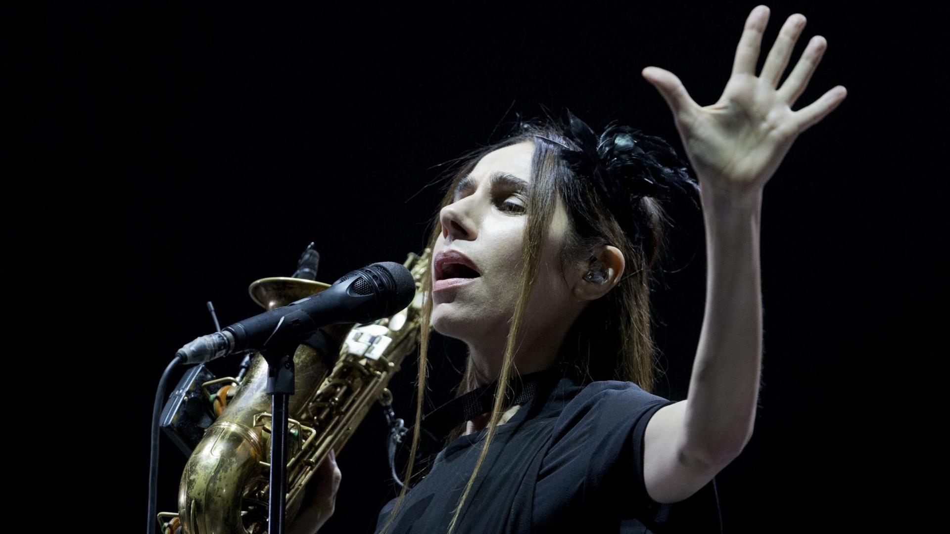 PJ Harvey steht vor einem Mikrophon mit einem Saxophon in der Hand. PJ Harvey steht vor einem Mikrophon mit einem Saxophon in der Hand.