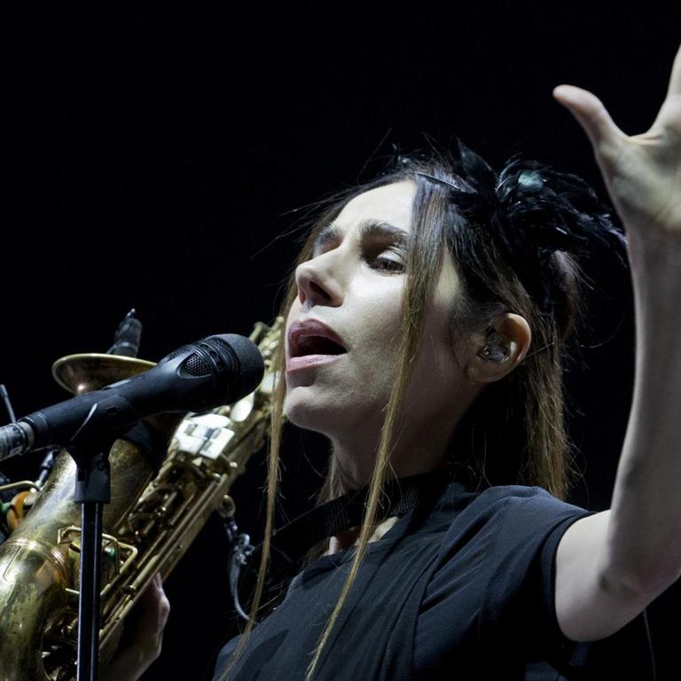 PJ Harvey steht vor einem Mikrophon mit einem Saxophon in der Hand. PJ Harvey steht vor einem Mikrophon mit einem Saxophon in der Hand.