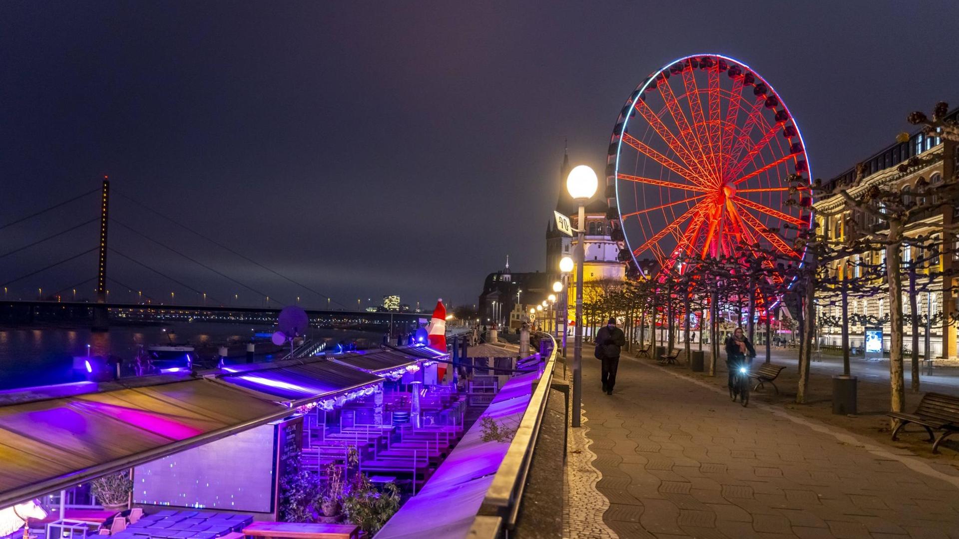 Blick auf die Düsseldorfer Altstadt mit Weihnachtsmarktständen, von denen viele geschlossen sind. Im Hintergrund ein rot leuchtendes Riesenrad. Blick auf die Düsseldorfer Altstadt mit Weihnachtsmarktständen, von denen viele geschlossen sind. Im Hintergrund ein rot leuchtendes Riesenrad.