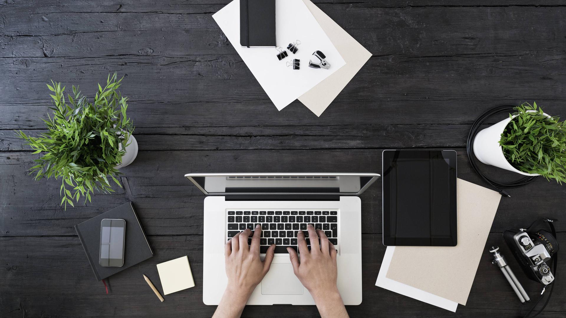 Von oben ist ein Notebook auf dem Tisch zu sehen, zwei Hände tippen auf der Tastatur. Von oben ist ein Notebook auf dem Tisch zu sehen, zwei Hände tippen auf der Tastatur.