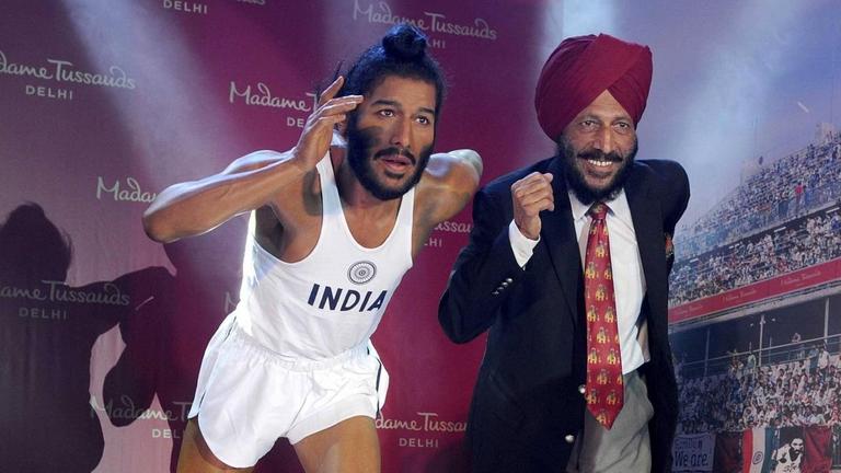 Milkha Singh steht freudig lachend neben seiner Wachsfigur, die ihn als jungen Laufsportler zeigt. Milkha Singh steht freudig lachend neben seiner Wachsfigur, die ihn als jungen Laufsportler zeigt.