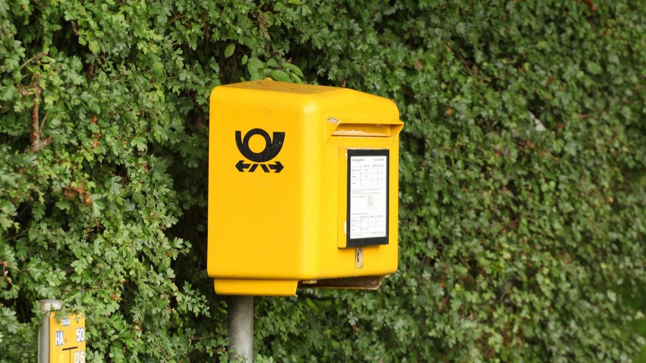 Ein Postkasten der Deutschen Post steht in Timmendorfer Strand vor einer grünen Hecke.