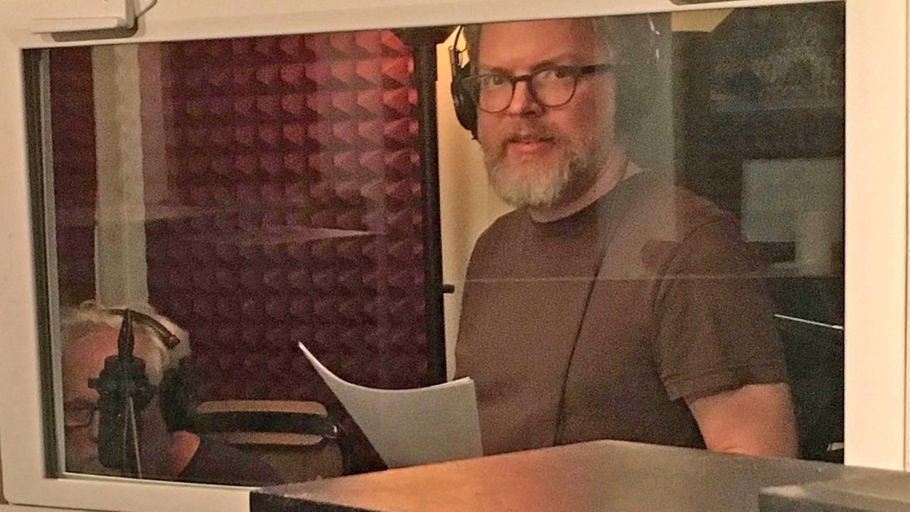 Jonathan Mitchell steht in einem Tonstudio und trägt einen Kopfhörer. Jonathan Mitchell steht in einem Tonstudio und trägt einen Kopfhörer.