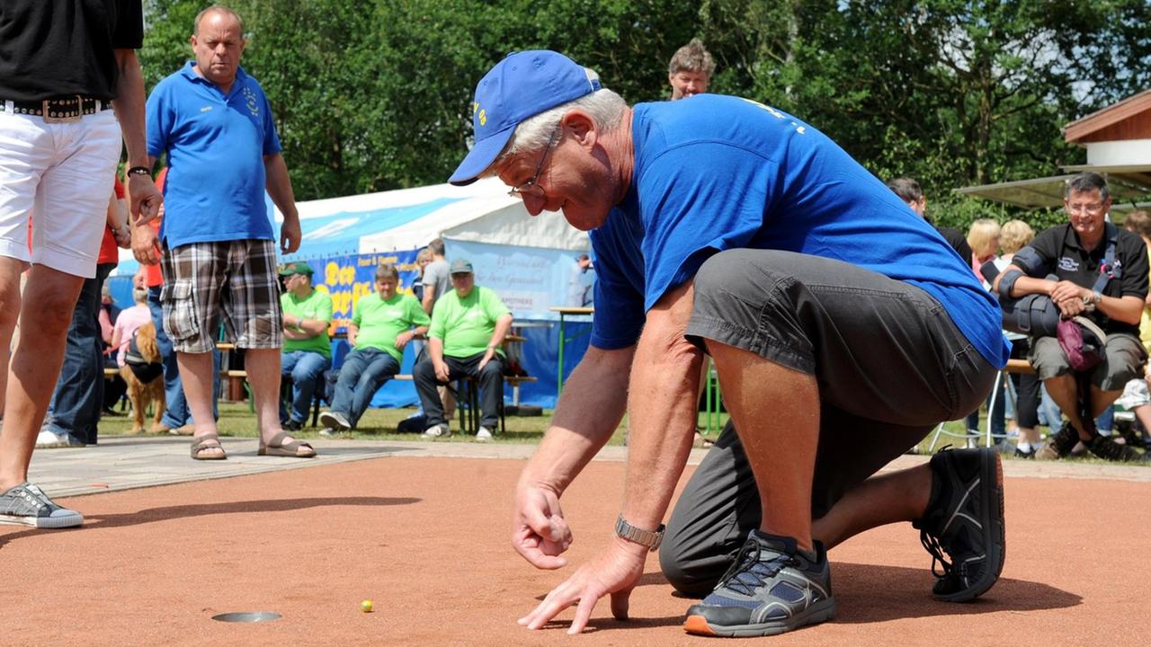 Ein Mann mit blauem T-Shirt stößt Murmeln auf einem rötlichen Sandplatz. Ein Mann mit blauem T-Shirt stößt Murmeln auf einem rötlichen Sandplatz.