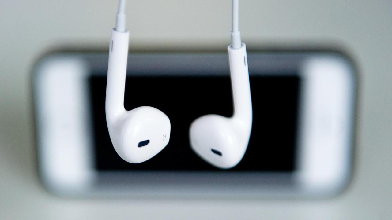 Kopfhörer hängen vor einem Apple Iphone.