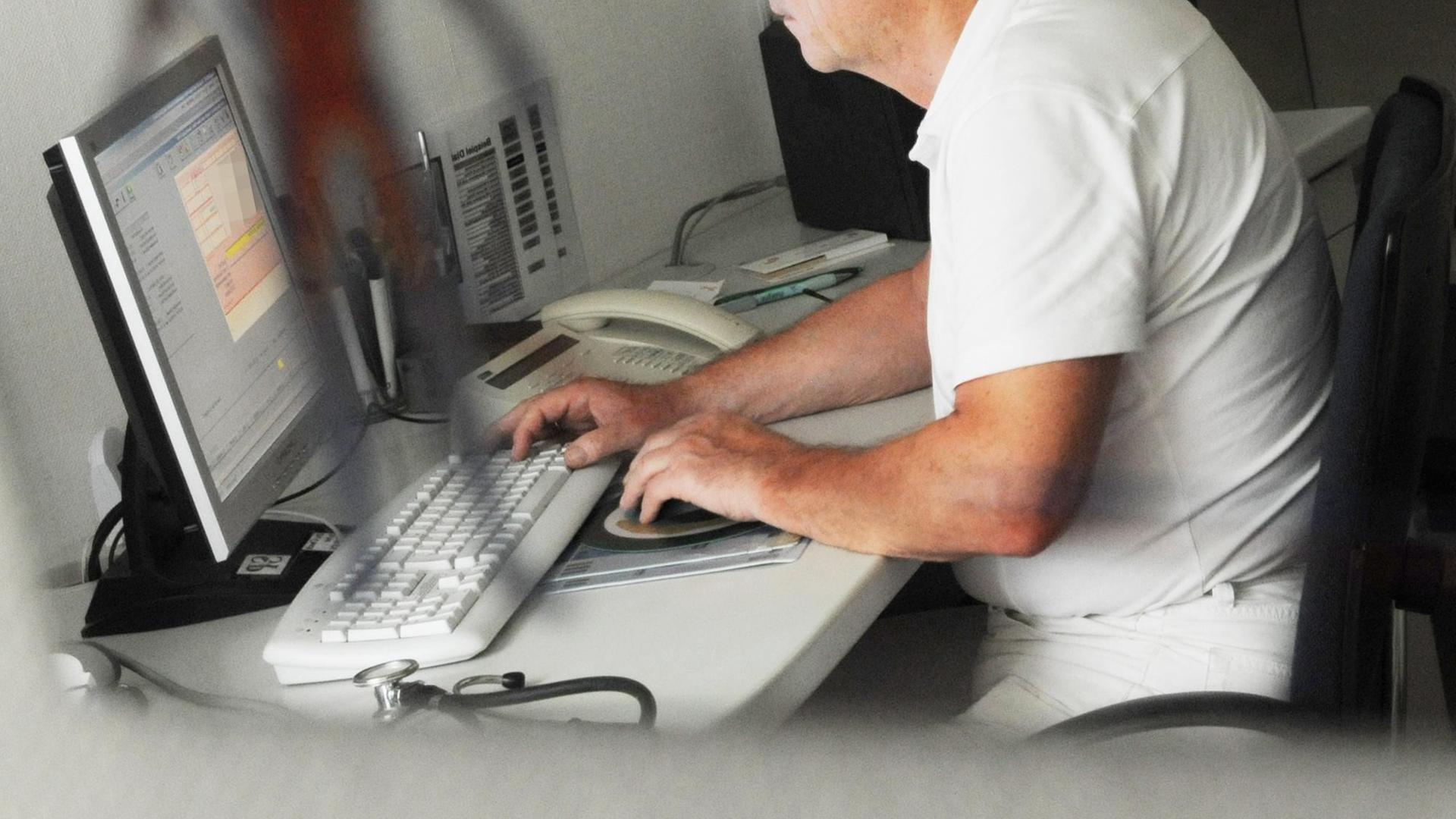 Ein Arzt sitzt in einer Praxis an einem Computer.