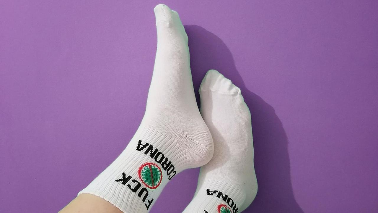 Ein paar Füsse mit weissen Socken und der Aufschrift "Fuck Corona" sind an eine violette Wand gelehnt. Ein paar Füsse mit weissen Socken und der Aufschrift "Fuck Corona" sind an eine violette Wand gelehnt.