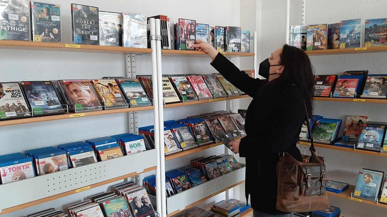 Eine Frau mit langen Haaren steht vor einem Regal in einer Bibliothek. Eine Frau mit langen Haaren steht vor einem Regal in einer Bibliothek.
