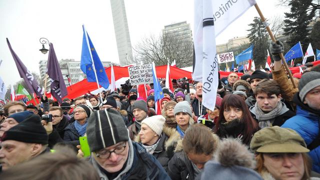 Eine Menschenmenge vor dem Parlamentsgebäude in Warschau hält Banner und Fahnen in die Höhe.