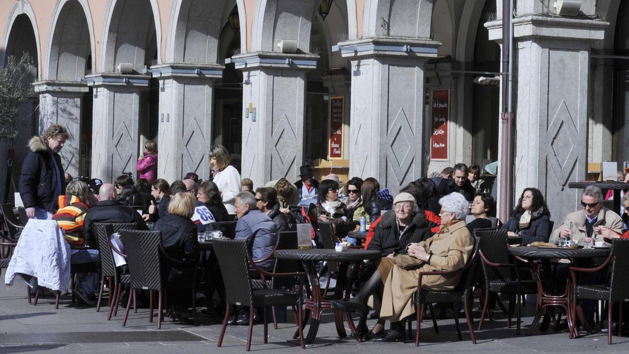 Menschen sitzen in einem Straßencafé in Bozen. Im Hintergrund ein Säulengang. Menschen sitzen in einem Straßencafé in Bozen. Im Hintergrund ein Säulengang.