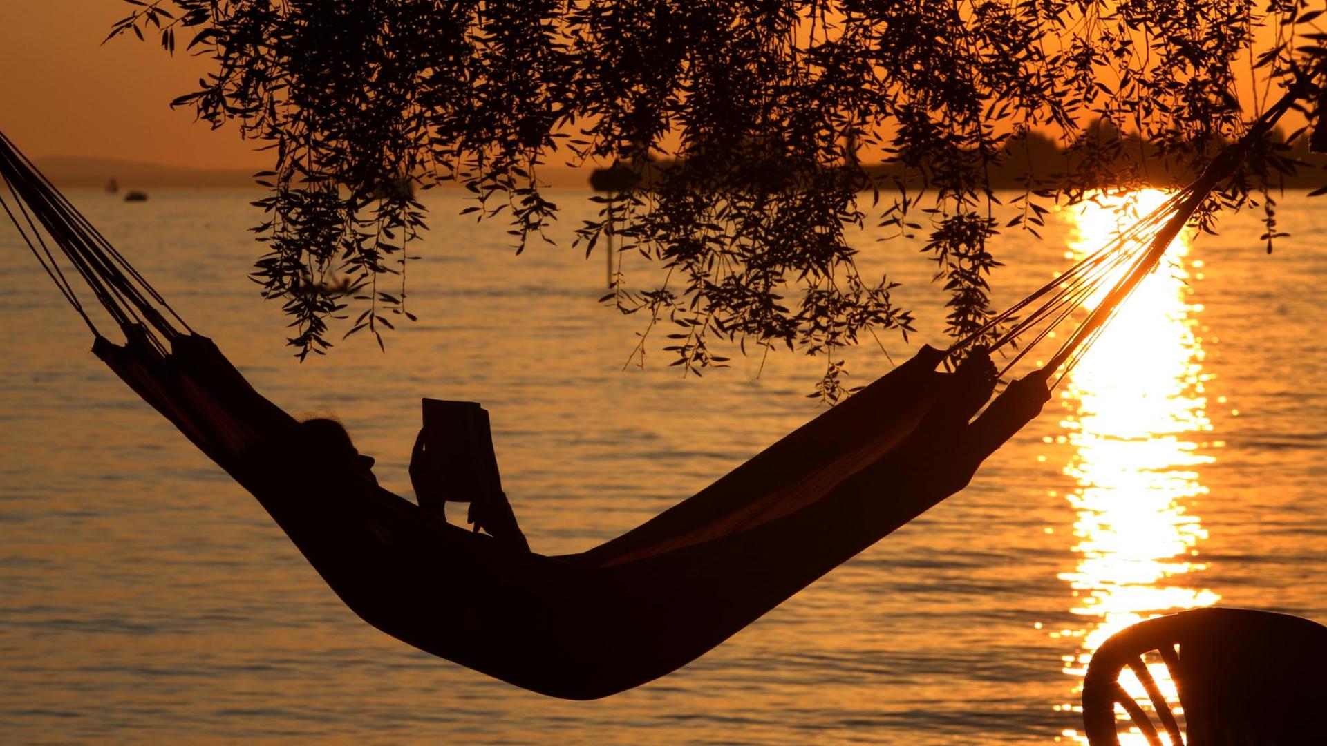 Eine Frau liest in einer Hängematte am Badestrand eines Campingplatzes in Lindau ein Buch. Eine Frau liest in einer Hängematte am Badestrand eines Campingplatzes in Lindau ein Buch.