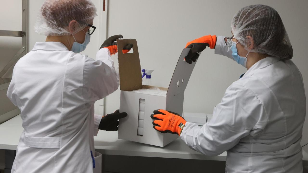 Mitarbeiter öffnen einen Karton mit einigen der ersten knapp 10.000 Dosen Corona-Impfstoff für Thüringen. Mitarbeiter öffnen einen Karton mit einigen der ersten knapp 10.000 Dosen Corona-Impfstoff für Thüringen.
