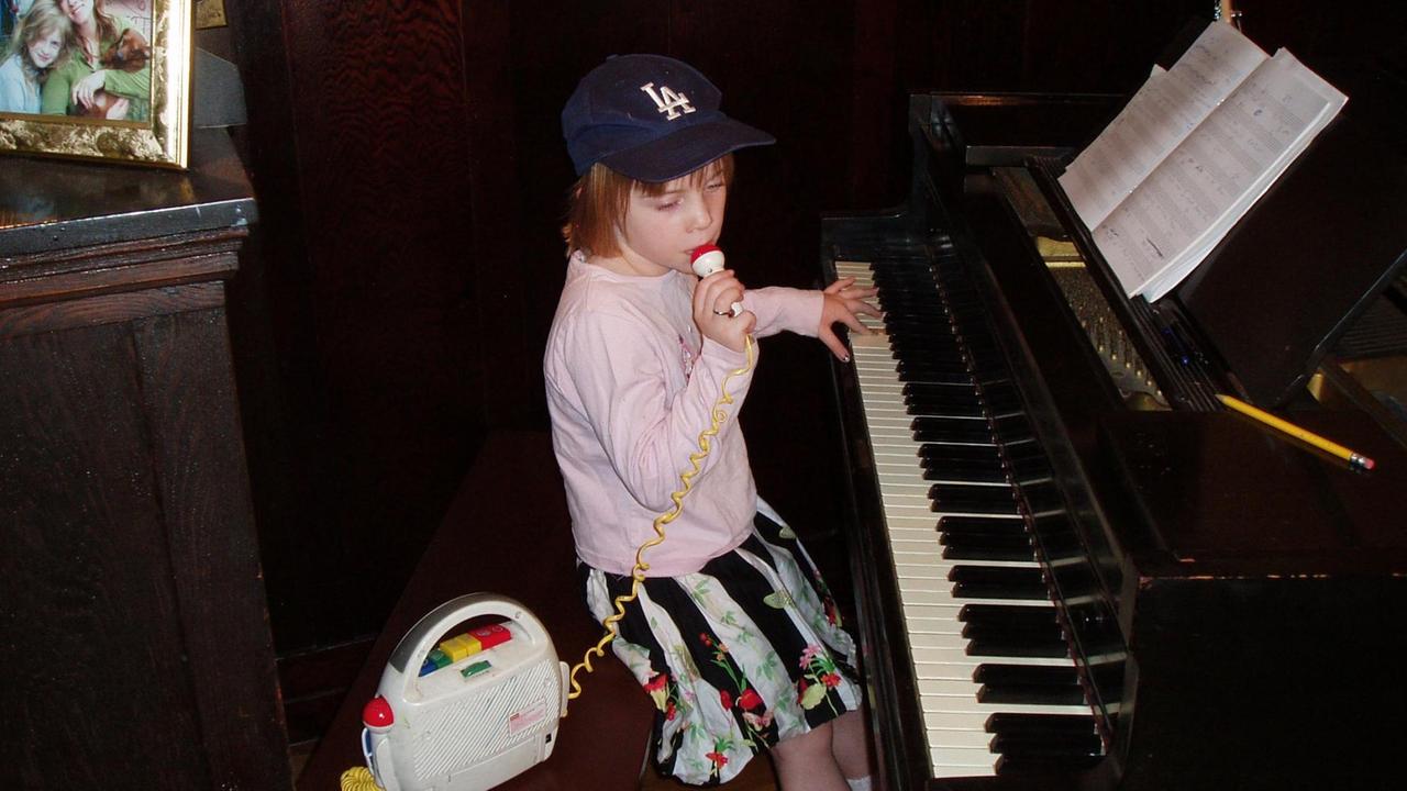Billie Eilish als Achtjährige, mit einer Hand am Klavier und mit der anderen am Mikrofon eines Kinderrekorders. Billie Eilish als Achtjährige, mit einer Hand am Klavier und mit der anderen am Mikrofon eines Kinderrekorders.