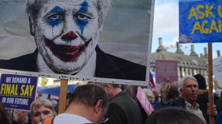 person holding sign with picture of a man wearing clown face art