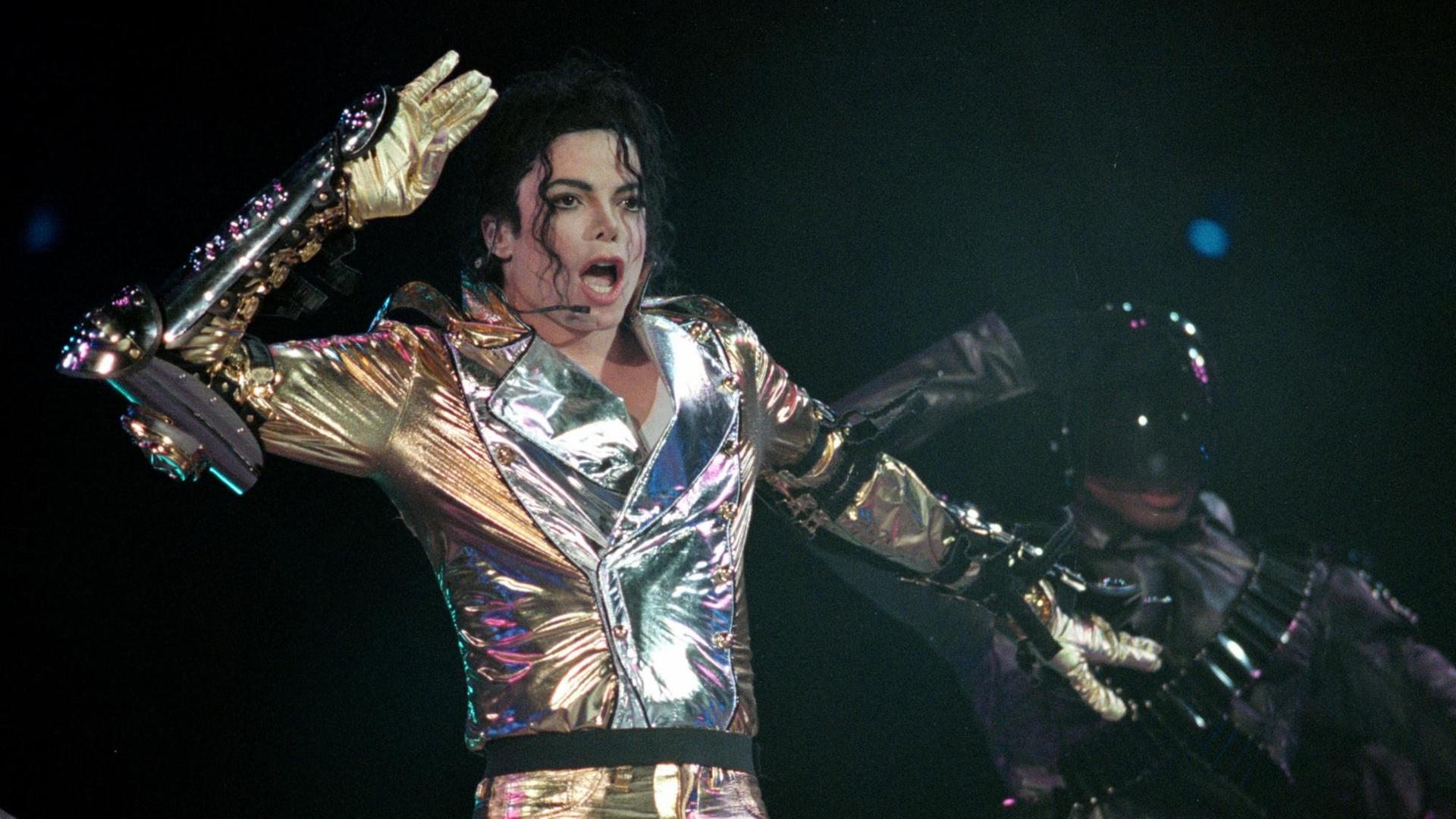 Michael Jackson steht in einem glitzernden Anzug auf der Bühne, tanzt und singt.