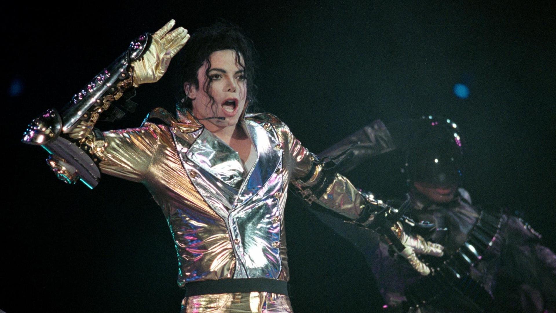 Michael Jackson steht in einem glitzernden Anzug auf der Bühne, tanzt und singt. Michael Jackson steht in einem glitzernden Anzug auf der Bühne, tanzt und singt.