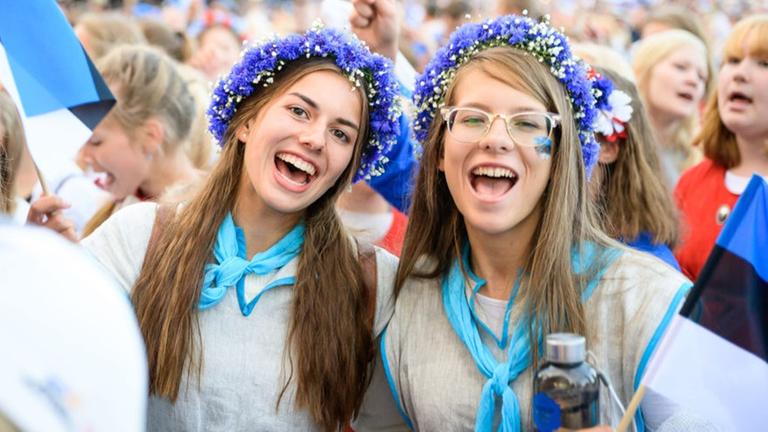 Zwei junge Estinnen mit typischem Blumenkranz und Trachtenbluse singen bei der Großveranstaltung. Zwei junge Estinnen mit typischem Blumenkranz und Trachtenbluse singen bei der Großveranstaltung.