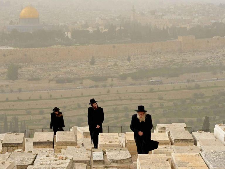 Ultra-orthodoxe Juden auf einem Friedhof auf dem Ölberg in Jerusalem, im Hintergrund der Felsendom.