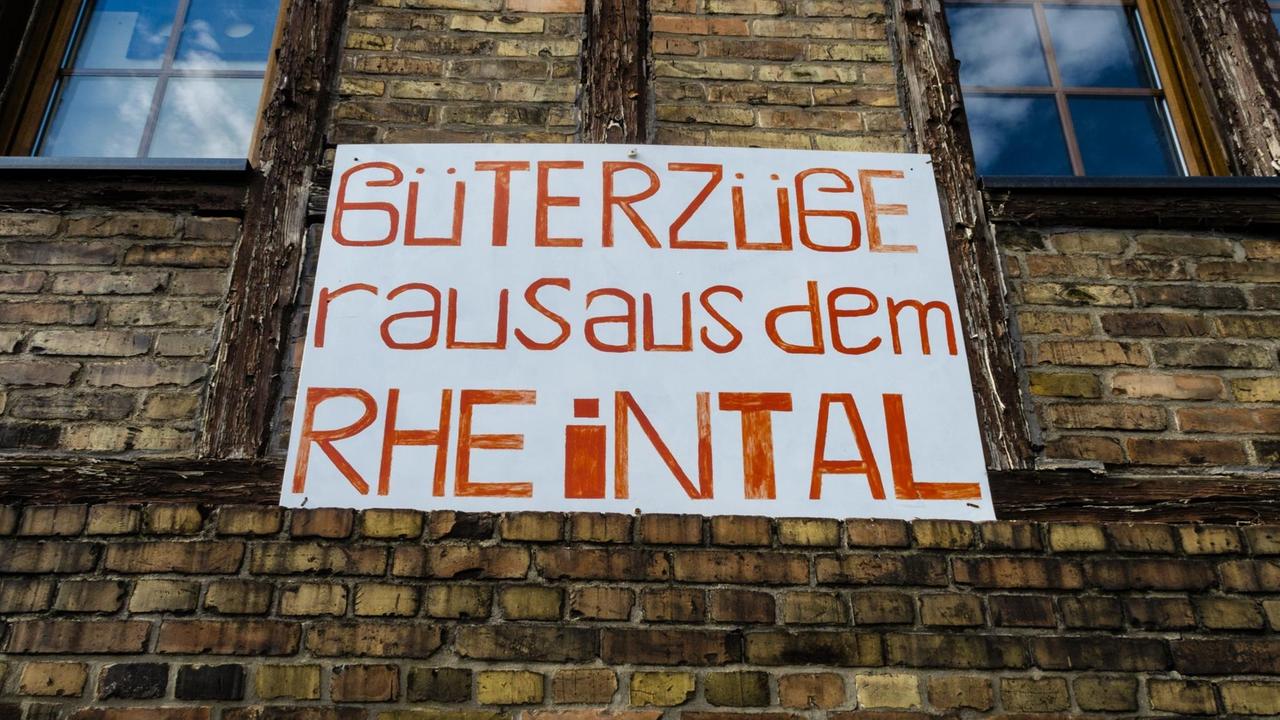 Ein Schild mit der Aufschrift "Güterzüge raus aus dem Rheintal" hängt in Kaub am Rhein an einem alten Haus mit Zigelsteinfassade.