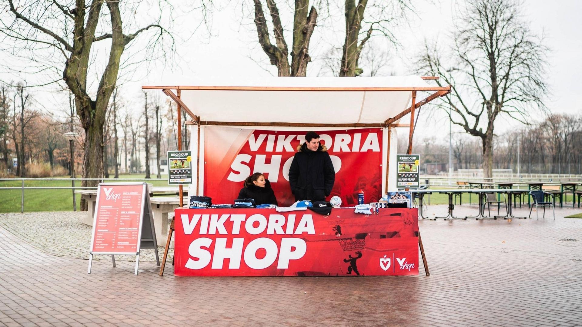 Ein Verkaufsstand mit Fanartikeln von Viktoria 89 vor dem Fußballplatz.