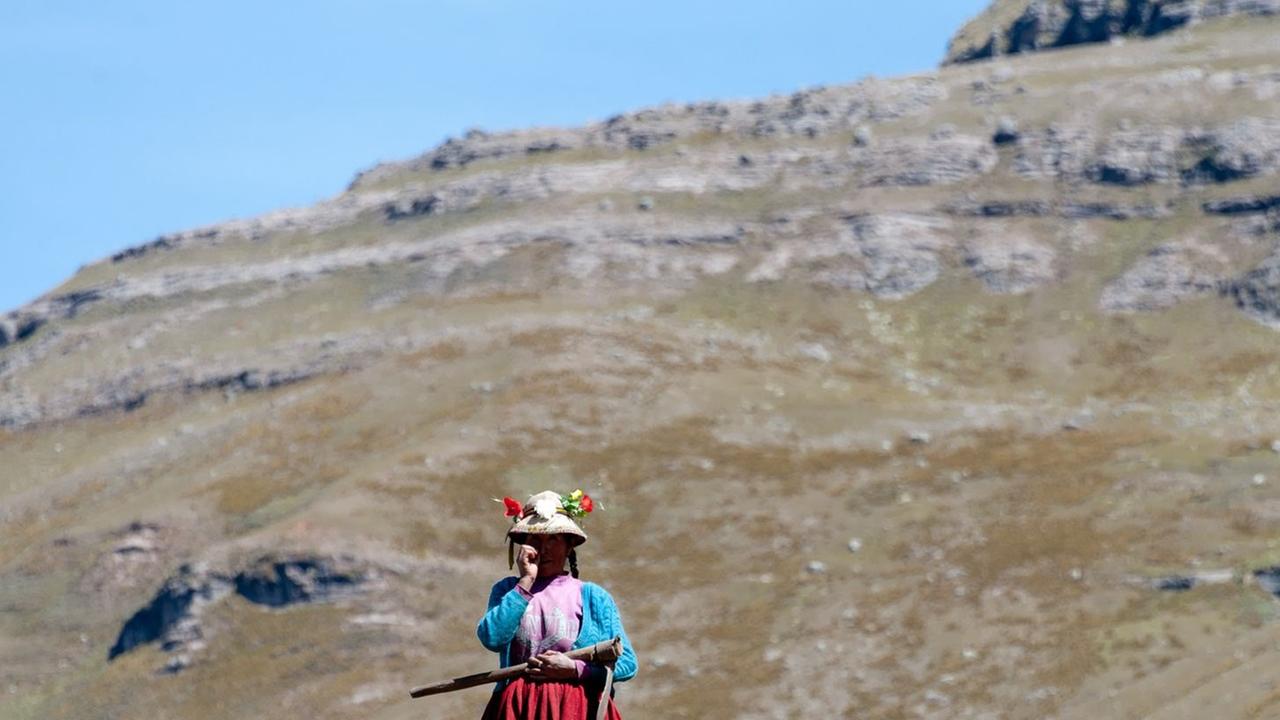 Eine Frau in traditioneller Kleidung steht vor einem Berpanorama in den peruanischen Anden. Eine Frau in traditioneller Kleidung steht vor einem Berpanorama in den peruanischen Anden.