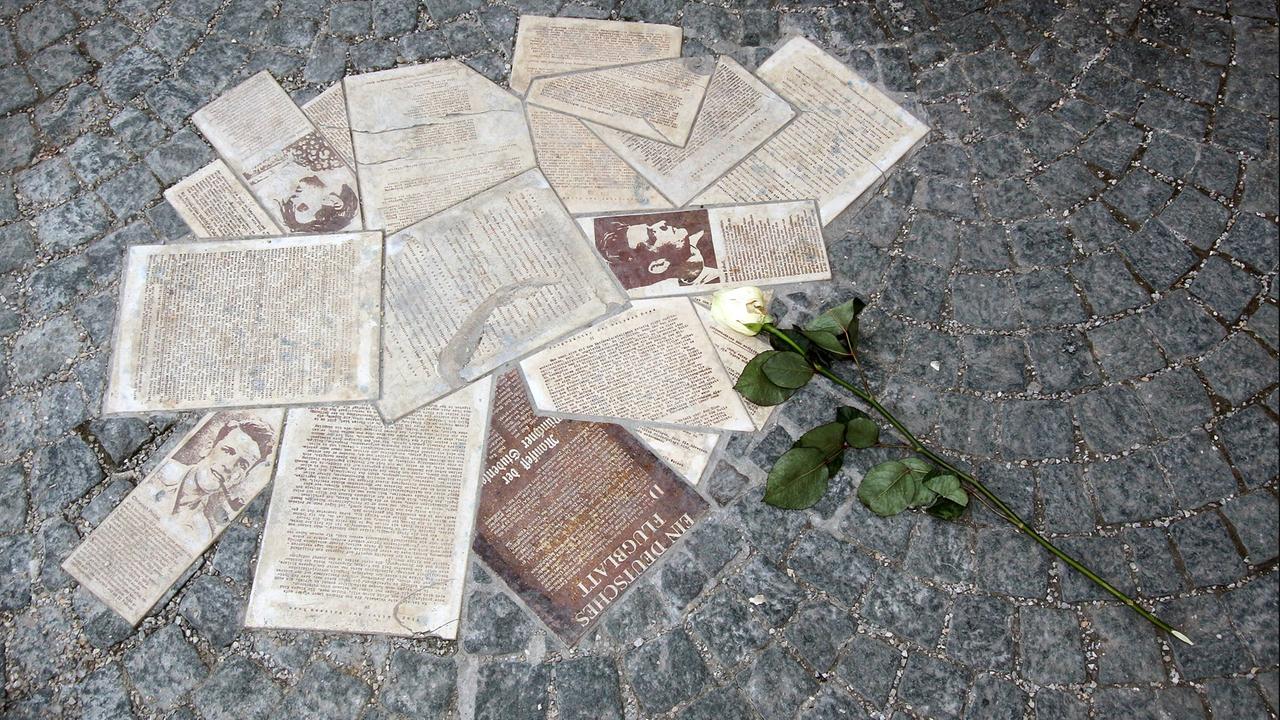In das Pflaster eingelassene Flugblätter mit Portrait von Hans Scholl und einer niedergelegten weißen Rose auf dem Campus der Ludwig Maximilian Universität München