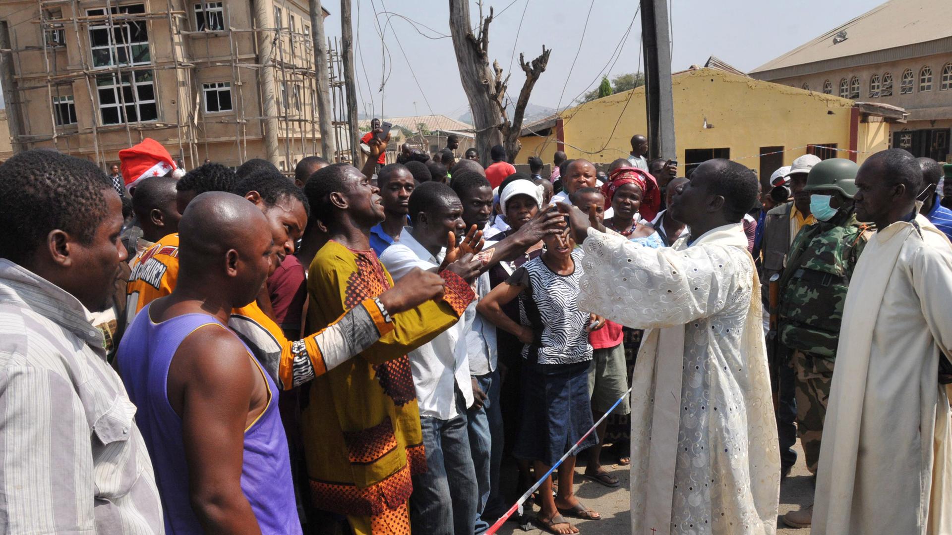 Pfarrer Issac Achi (r) versucht vor der Katholischen Kirche St. Theresa in Madalla (Nigeria) die Menschenmenge zu beruhigen Pfarrer Issac Achi (r) versucht vor der Katholischen Kirche St. Theresa in Madalla (Nigeria) die Menschenmenge zu beruhigen