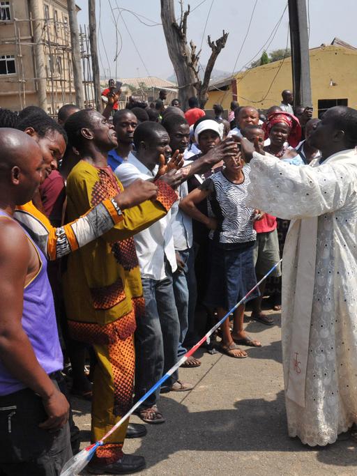 Pfarrer Issac Achi (r) versucht vor der Katholischen Kirche St. Theresa in Madalla (Nigeria) die Menschenmenge zu beruhigen