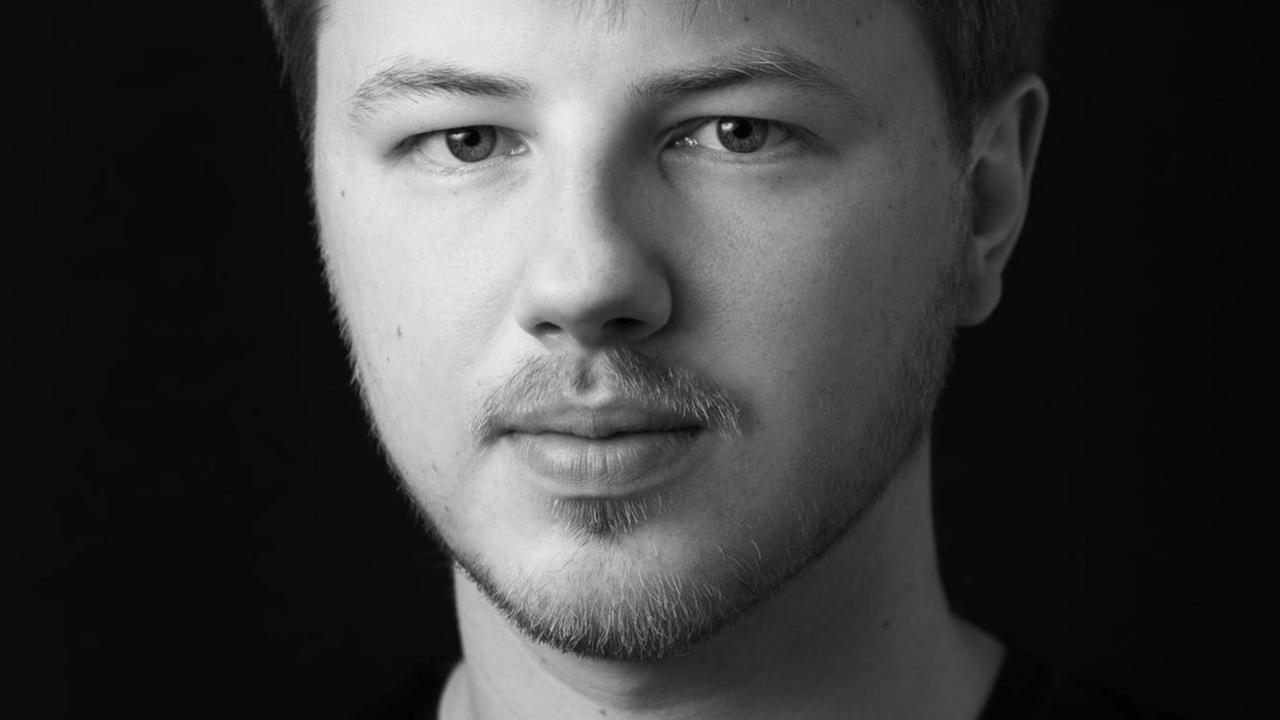 Ein junger Mann mit kurzem Haar und gepflegtem Dreitagebart blickt auf einem schwarz-weiß-Foto ernsthaft in die Kamera. Ein junger Mann mit kurzem Haar und gepflegtem Dreitagebart blickt auf einem schwarz-weiß-Foto ernsthaft in die Kamera.
