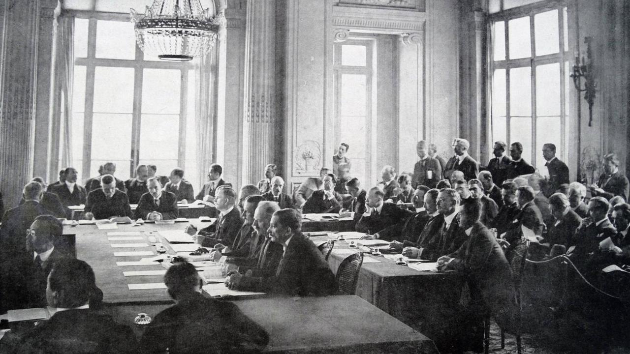 Vertragsverhandlungen in Versailles im Mai 1919. Mehrere Delegationen sitzen in einem großen Saal des Schlosses. Vertragsverhandlungen in Versailles im Mai 1919. Mehrere Delegationen sitzen in einem großen Saal des Schlosses.