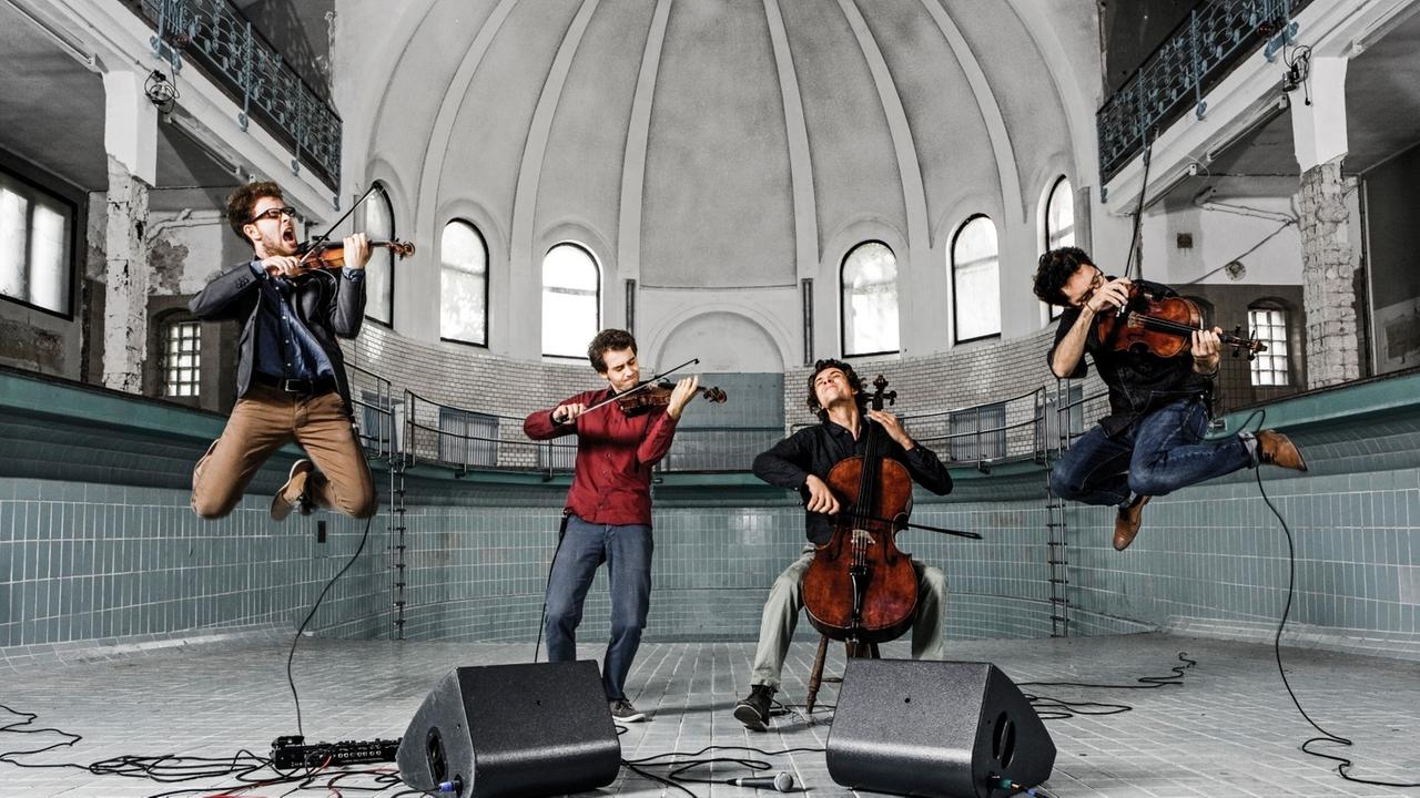 Die vier Musiker spielen in einem leeren Schwimmbecken und springen dabei in die Luft. Die vier Musiker spielen in einem leeren Schwimmbecken und springen dabei in die Luft.
