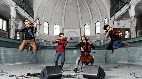 Die vier Musiker spielen in einem leeren Schwimmbecken und springen dabei in die Luft.