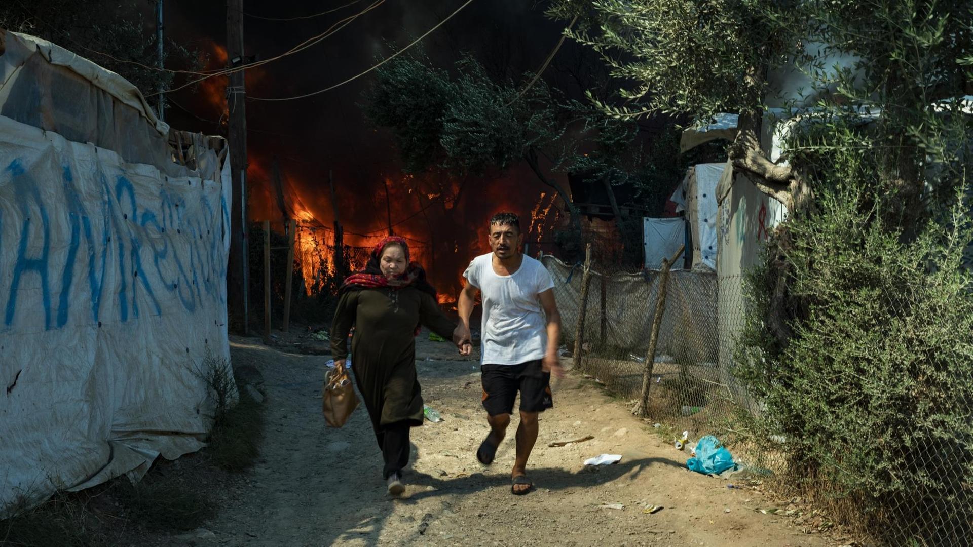 Ein rennedes Paar flieht vor den Flammen und dem Feuer, das im Flüchtlingslager Moria ausgebrochen ist. Ein rennedes Paar flieht vor den Flammen und dem Feuer, das im Flüchtlingslager Moria ausgebrochen ist.