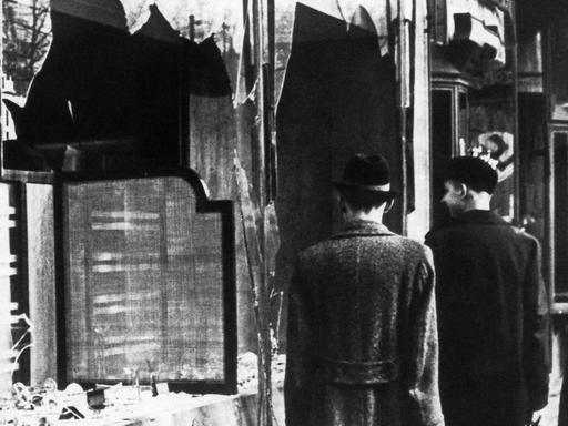 Passanten vor einer zerstörten Fensterfront eines jüdischen Geschäfts in Berlin nach der Reichspogromnacht 1938.