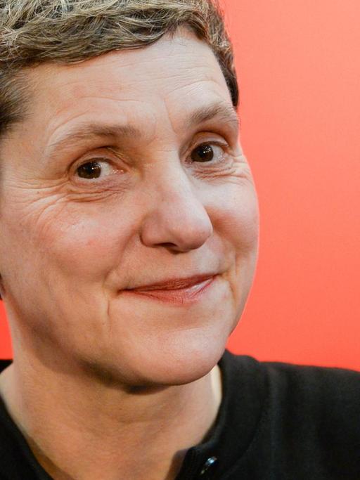 Die Autorin Felicitas Hoppe lächtelt vor einem roten Hintergrund seitlich in die Kamera