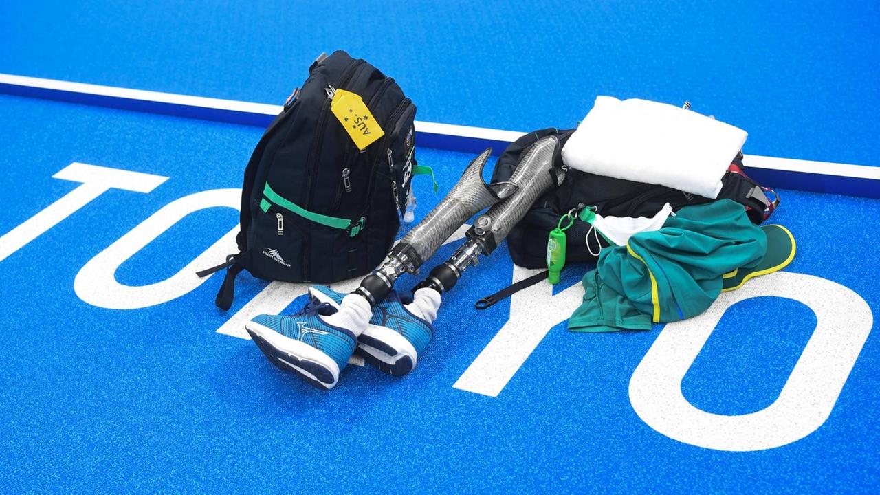 Auf blauem Untergrund mit dem weißen Schriftzug Tokio liegen ein Rucksack, ein Handtuch, Schwimmkleidung und zwei Beinprothesen. Auf blauem Untergrund mit dem weißen Schriftzug Tokio liegen ein Rucksack, ein Handtuch, Schwimmkleidung und zwei Beinprothesen.