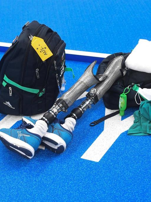 Auf blauem Untergrund mit dem weißen Schriftzug Tokio liegen ein Rucksack, ein Handtuch, Schwimmkleidung und zwei Beinprothesen.
