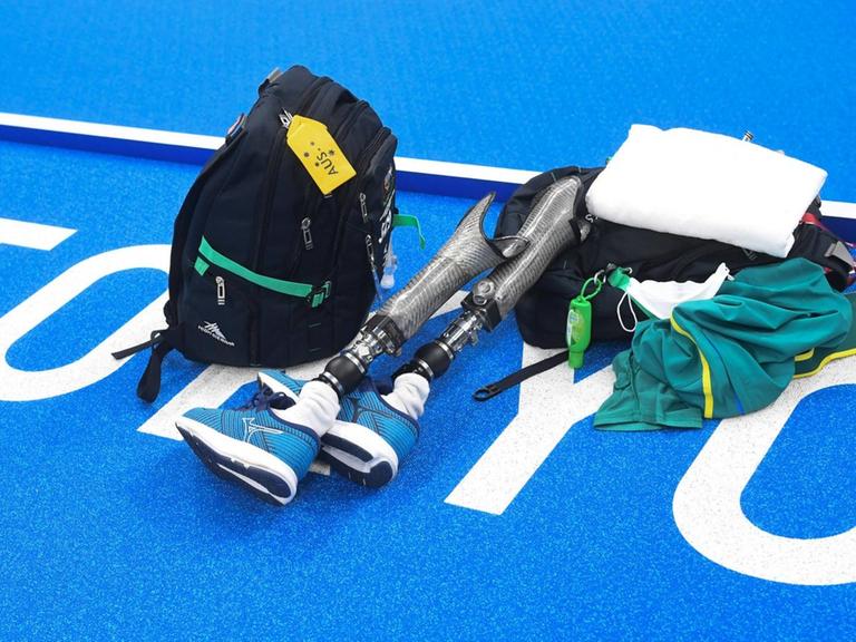Auf blauem Untergrund mit dem weißen Schriftzug Tokio liegen ein Rucksack, ein Handtuch, Schwimmkleidung und zwei Beinprothesen.
