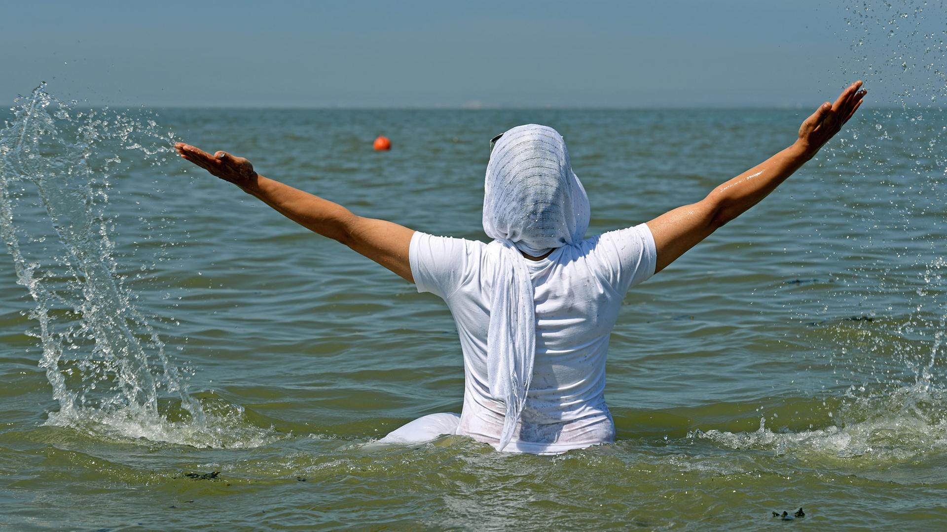 Eine Frau mit Kopftuch und T-Shirt badet am 21.07.2016 am Strand von Norddeich (Niedersachsen) in der Nordsee. Eine Frau mit Kopftuch und T-Shirt badet am 21.07.2016 am Strand von Norddeich (Niedersachsen) in der Nordsee.