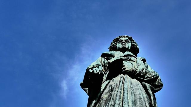 Blick hinauf am Beethovendenkmal in Bonn am Rhein, wo die grau-grüne Bronzefigur in den blauen Himmel ragt.