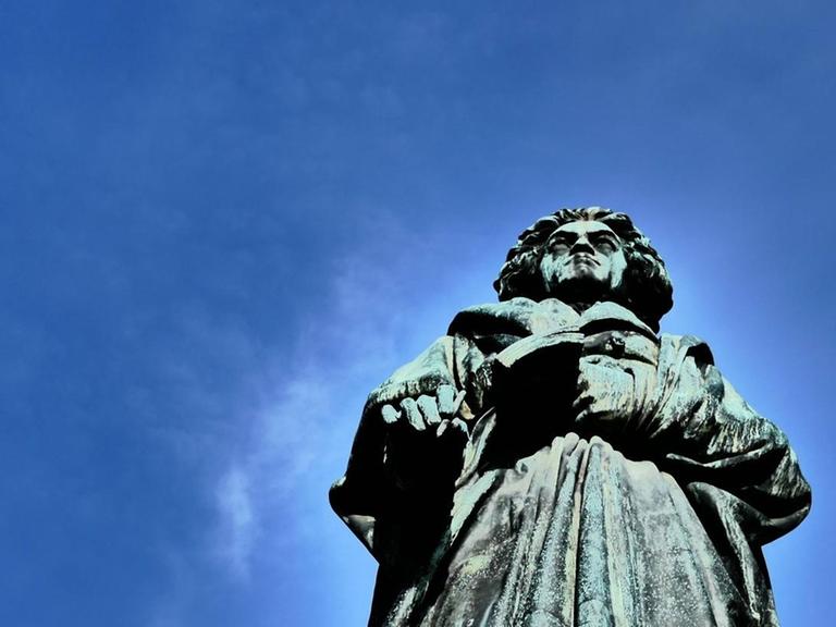 Blick hinauf am Beethovendenkmal in Bonn am Rhein, wo die grau-grüne Bronzefigur in den blauen Himmel ragt.