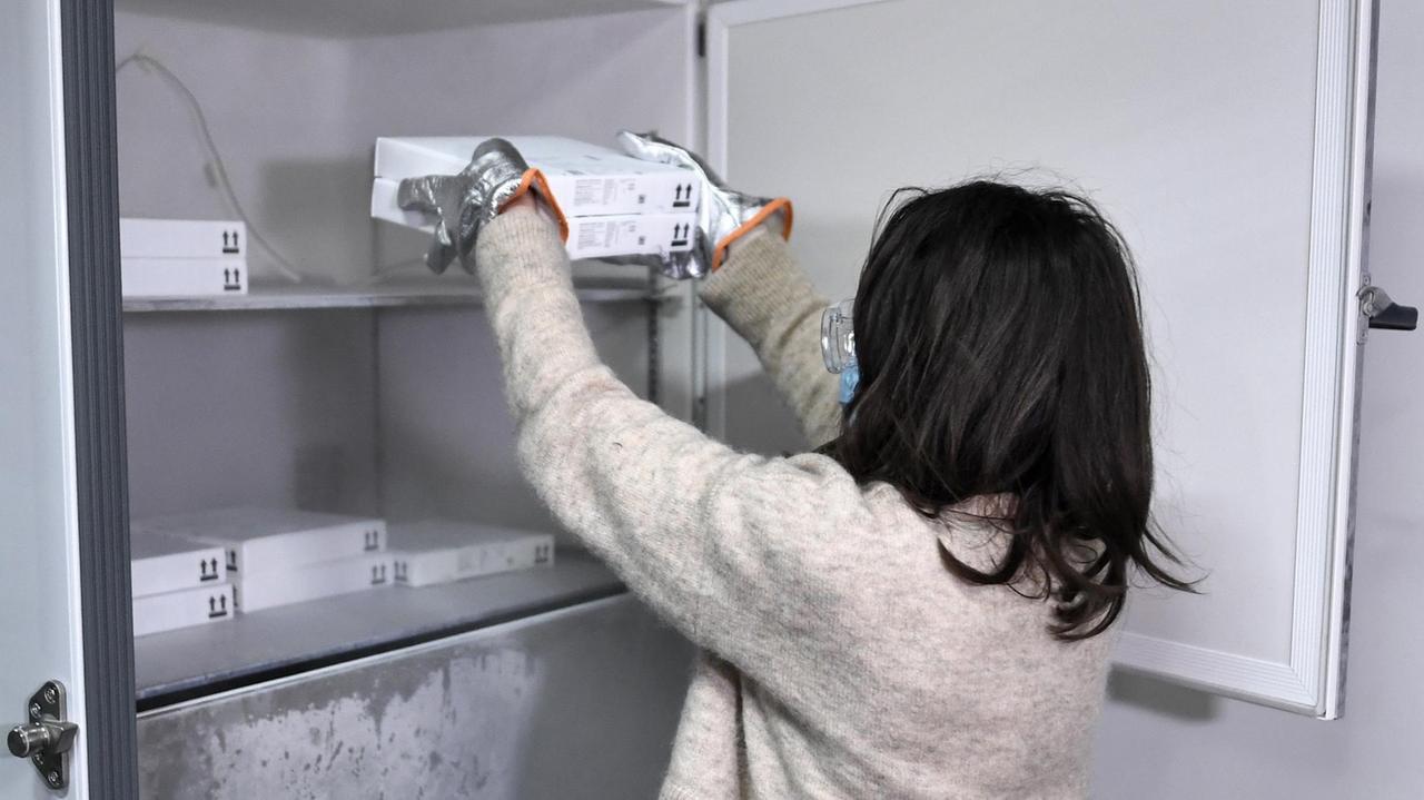 Eine Mitarbeiterin legt ein weißes Paket in einen speziellen Tiefkühlschrank. Eine Mitarbeiterin legt ein weißes Paket in einen speziellen Tiefkühlschrank.