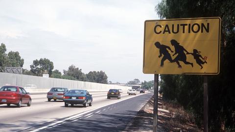 Ein Verkehrsschild an einer stark befahrenen Straße entlang der Grenze zwischen San Diego in den USA und Tijuana in Mexiko mahnt zur Vorsicht vor flüchtenden Mexikanern, die auf ihrem Weg in die Staaten plötzlich die Straße überqueren könnten und ein Unfallrisiko darstellen.