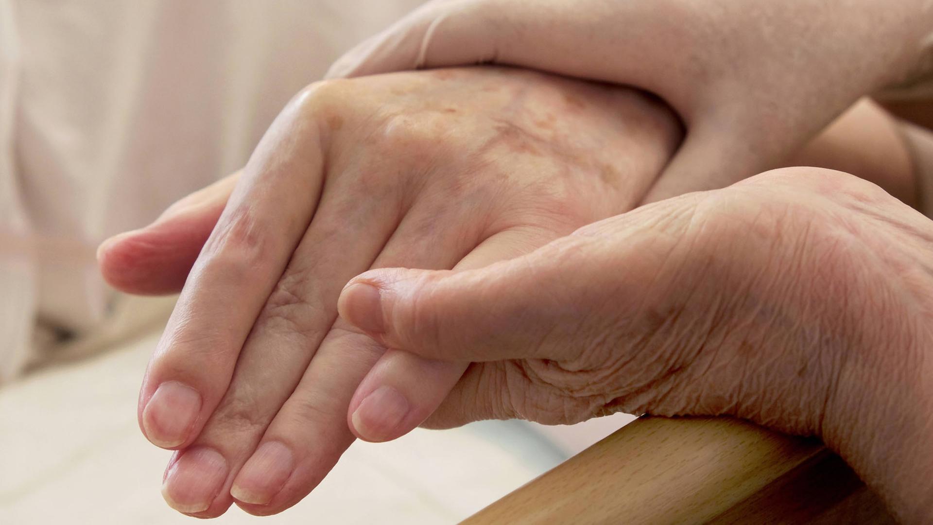 Pflege von Demenzkranken: Ein Paar Hände hält die Hand eines älteren Menschen. Pflege von Demenzkranken: Ein Paar Hände hält die Hand eines älteren Menschen.