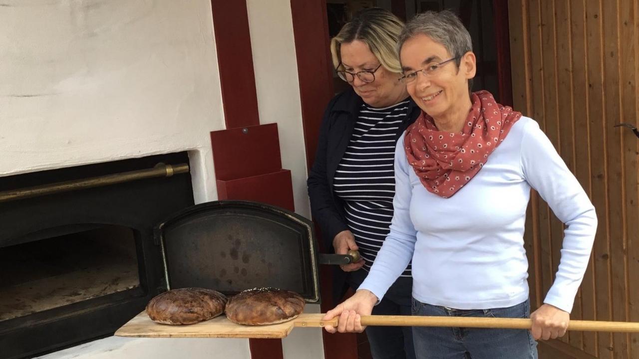 Zwei Bäckerinnen holen zwei Brotlaibe aus dem Ofen. Zwei Bäckerinnen holen zwei Brotlaibe aus dem Ofen.