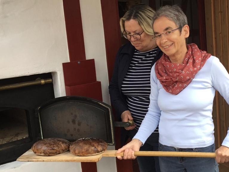 Zwei Bäckerinnen holen zwei Brotlaibe aus dem Ofen.